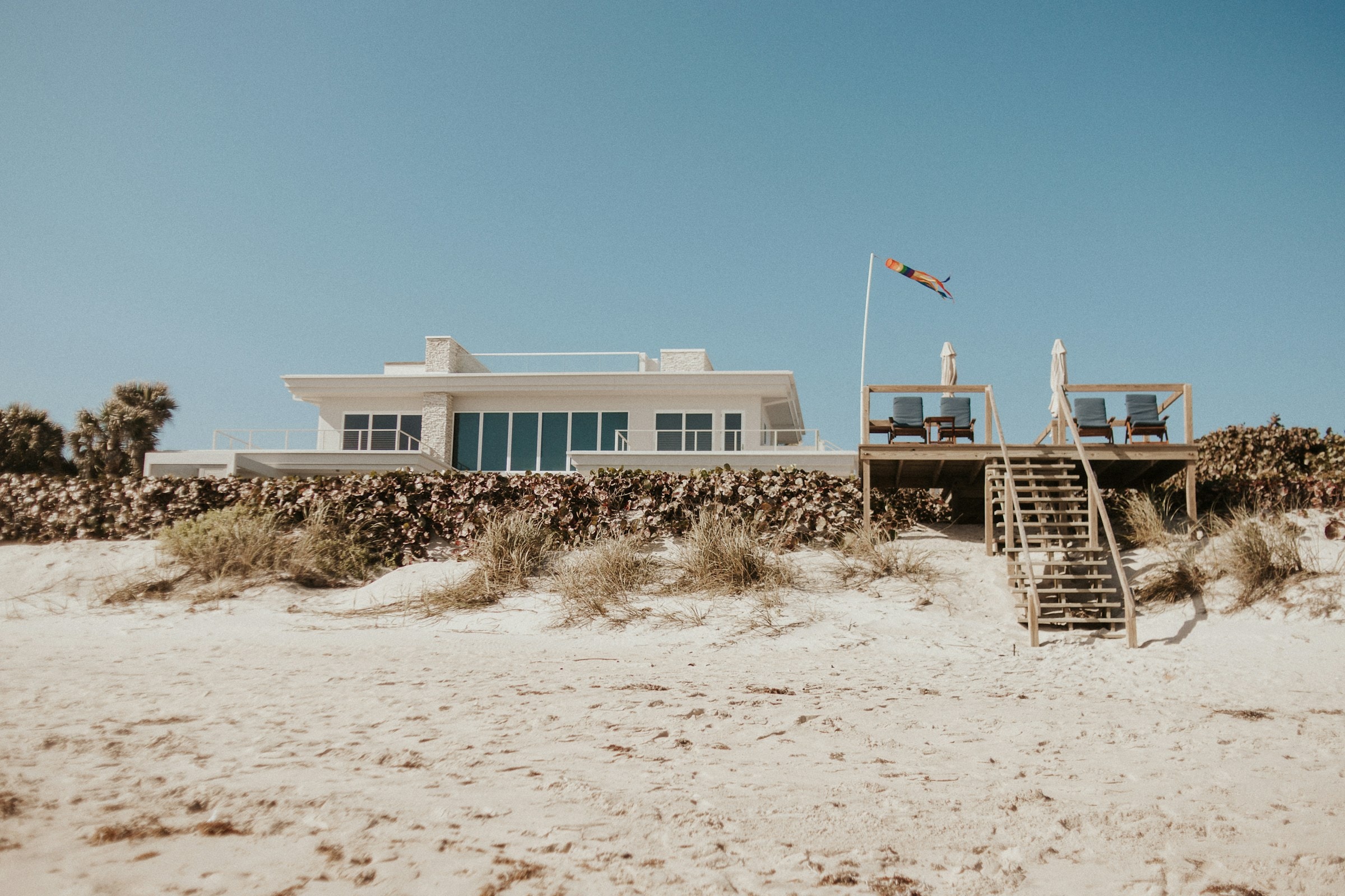 A modern white beachfront home above the dunes, with a private stairway to the sand. Illustrative architecture, not a current listing.