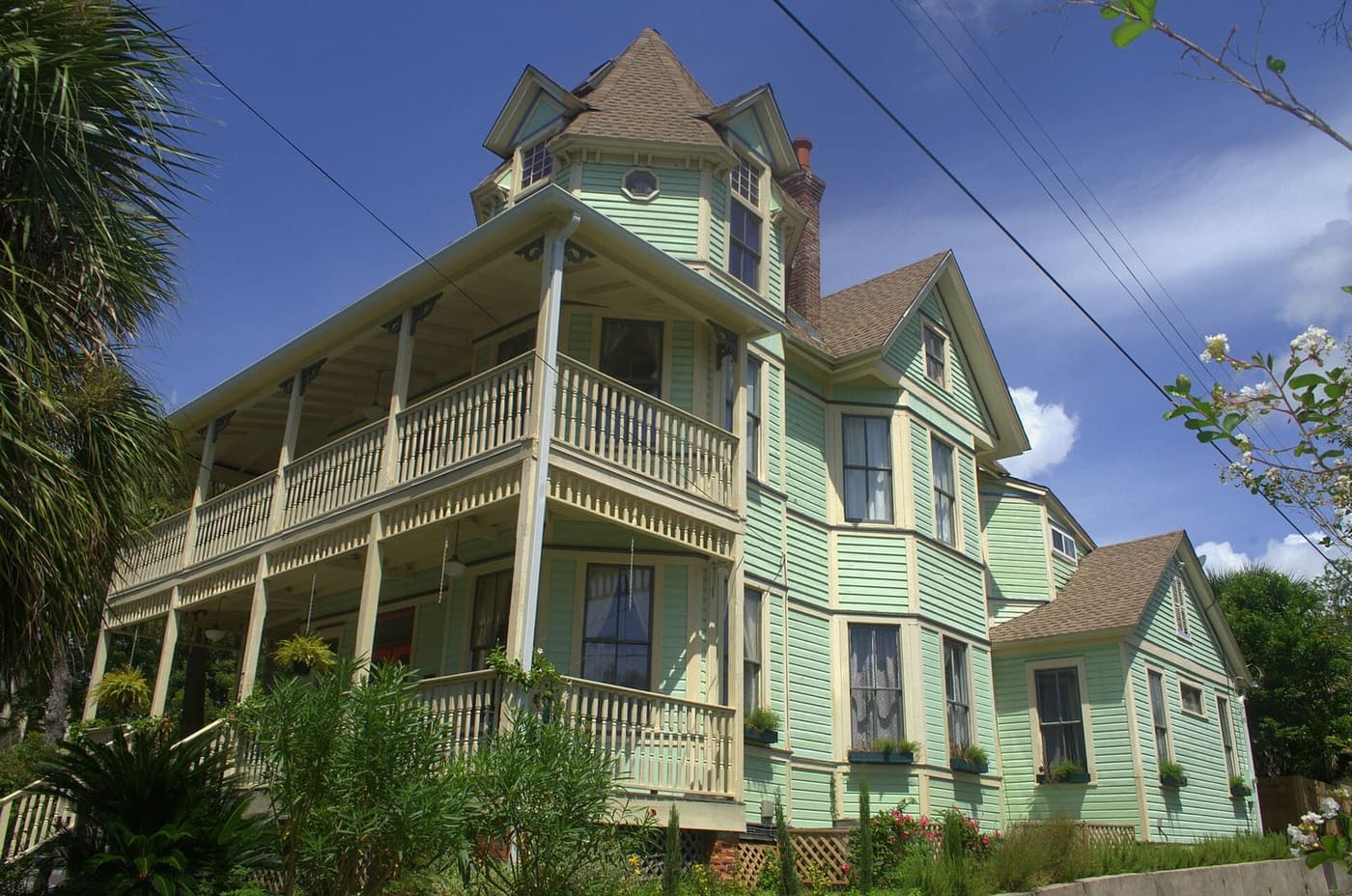 Marzoni House in Pensacola with green siding, a turret and two levels of porches